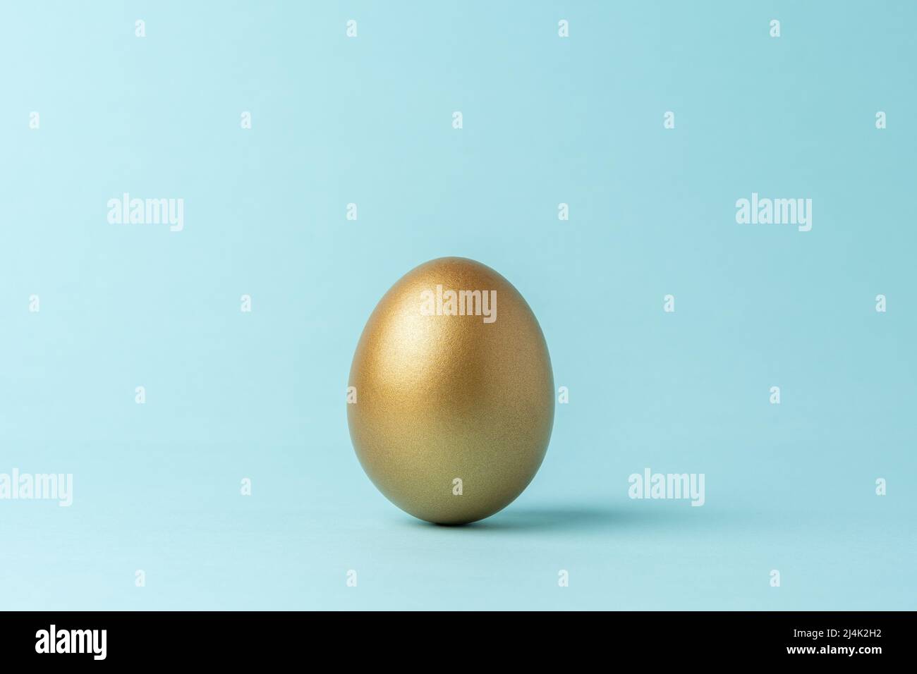 Golden Easter egg on blue background. Easter minimal concept. Creative Happy Easter or spring layout. Stock Photo