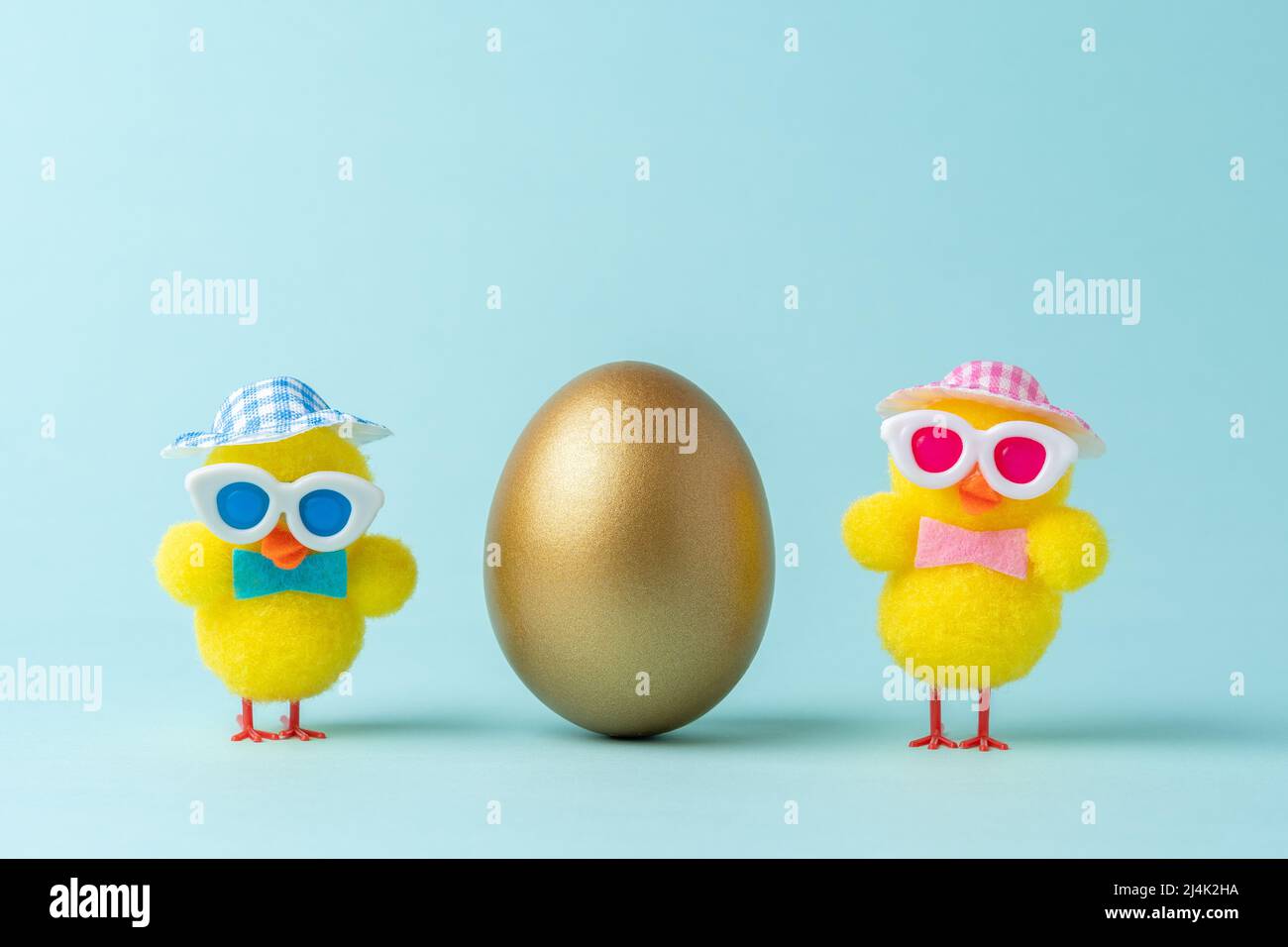 Creative composition with gold Easter egg and chickens on blue background. Minimal Easter background. Spring holidays concept. Stock Photo