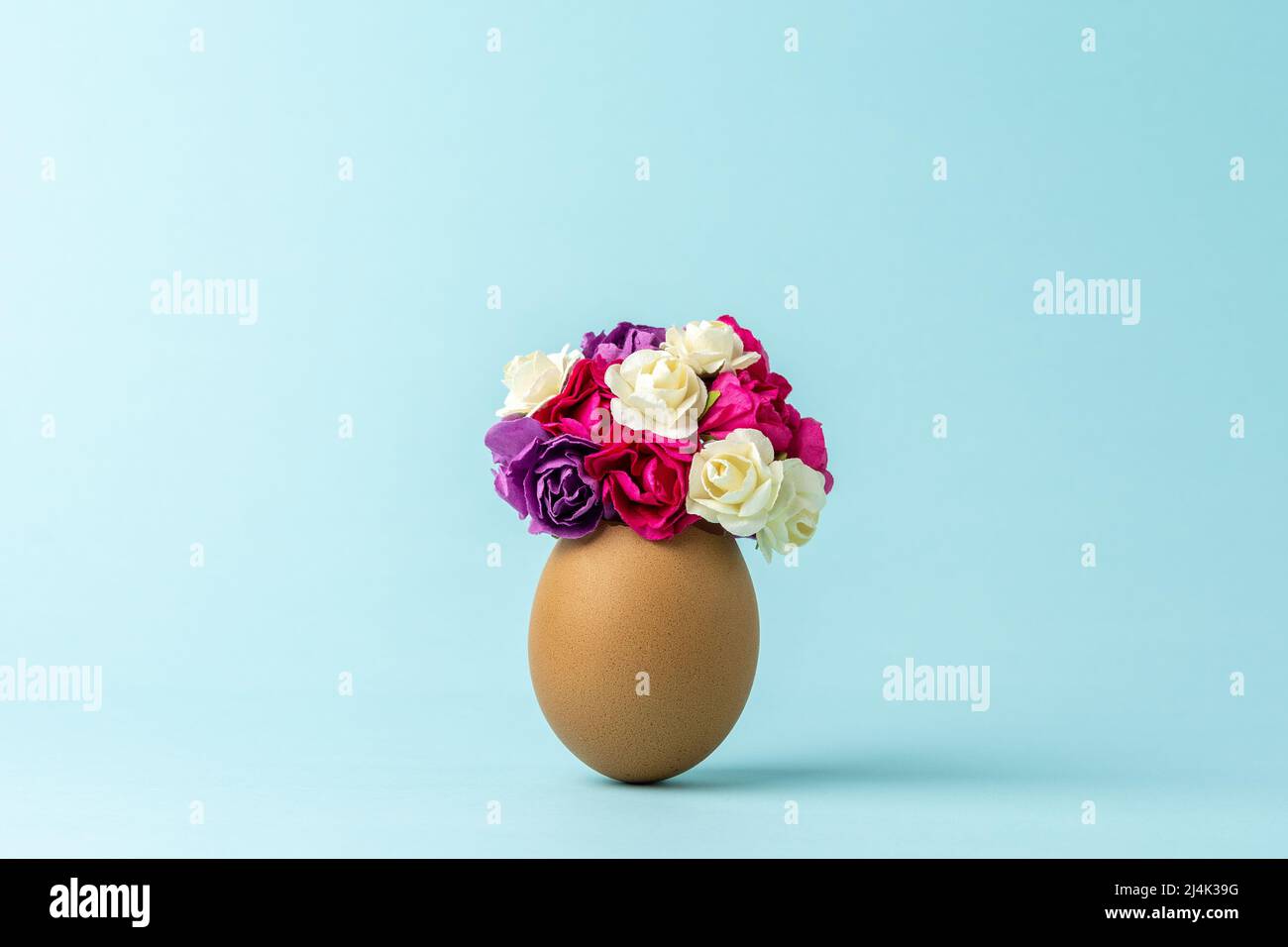 Spring flowers in cracked eggshell against pastel blue background. Easter minimal concept. Creative Happy Easter or spring layout. Stock Photo