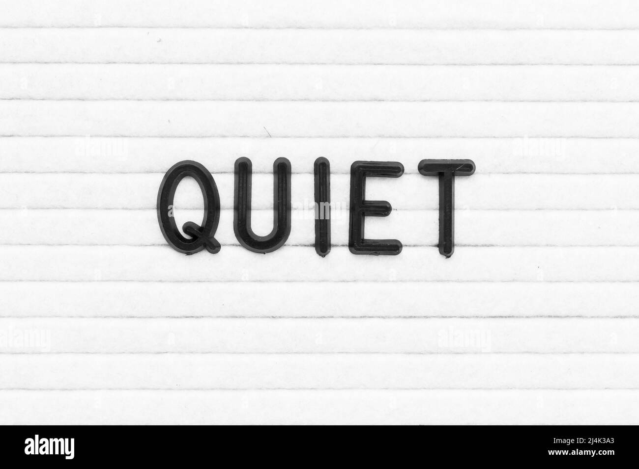 Black color letter in word quiet on white felt board background Stock