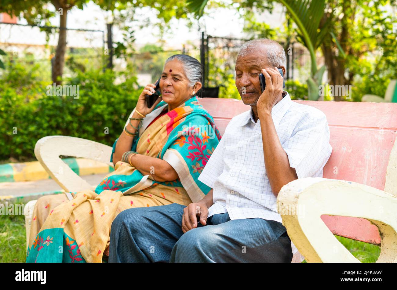Senior couple busy talking on mobile phone while sitting on park ...