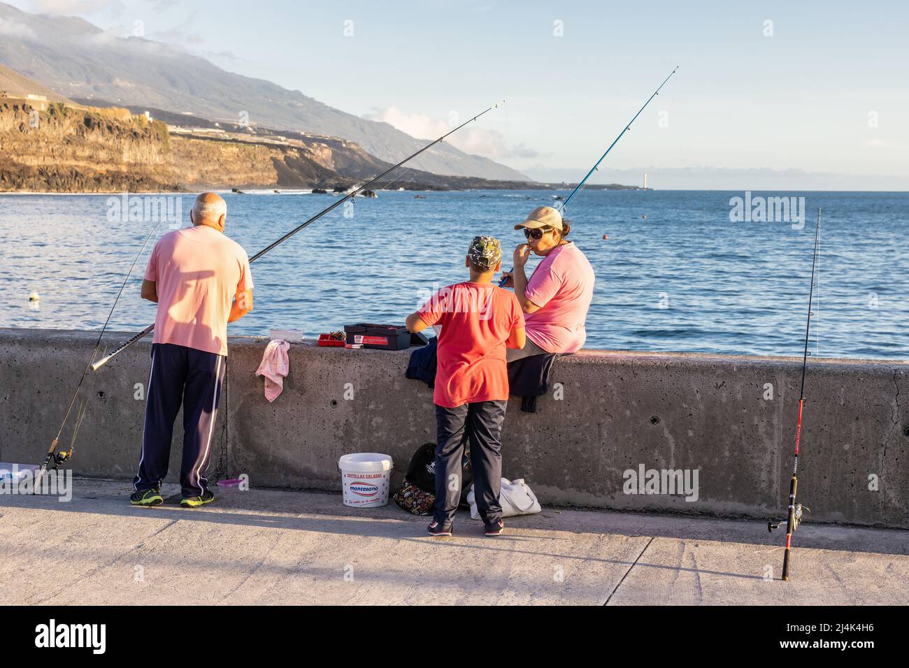 Tazacorte, Spain - March 02, 2022: Three people with fishing-rods at pier near harbor Tazacorte , La Palma Island Stock Photo