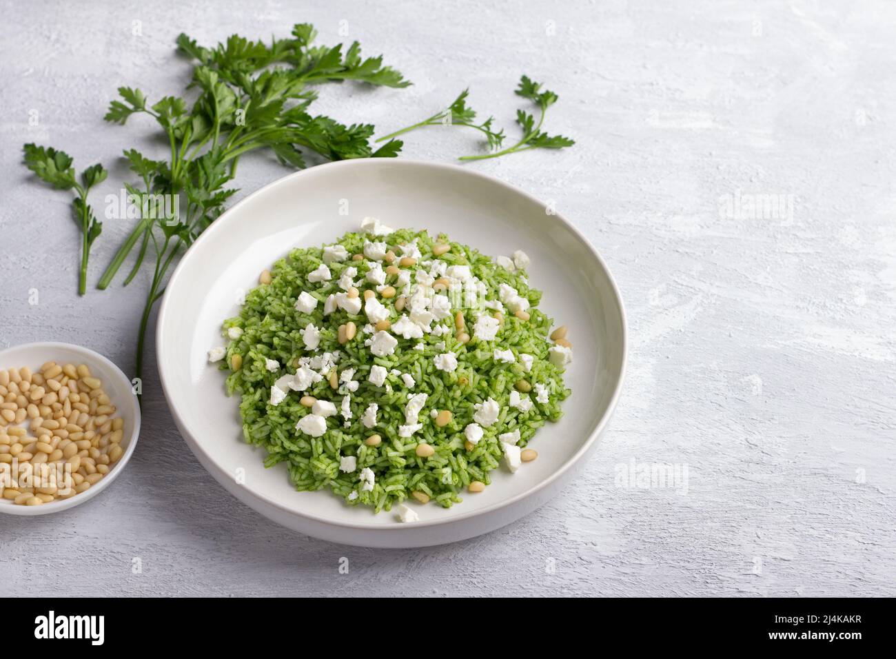Plate of green rice with pine nuts, feta cheese and parsley on a gray background, free space. healthy vegetarian food Stock Photo