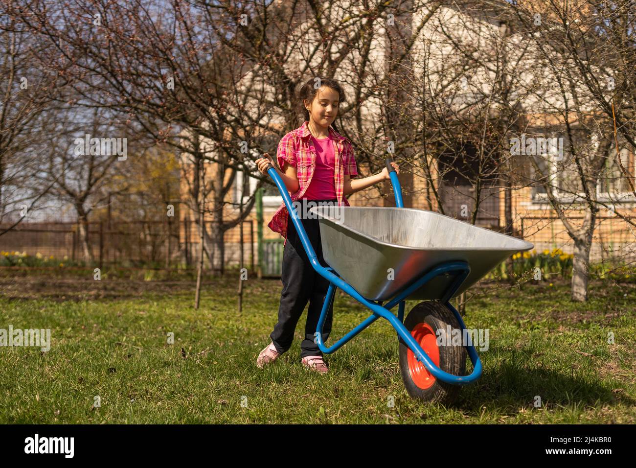 Adorable girl pushing wheelbarrow on a farm. Farming and gardening for