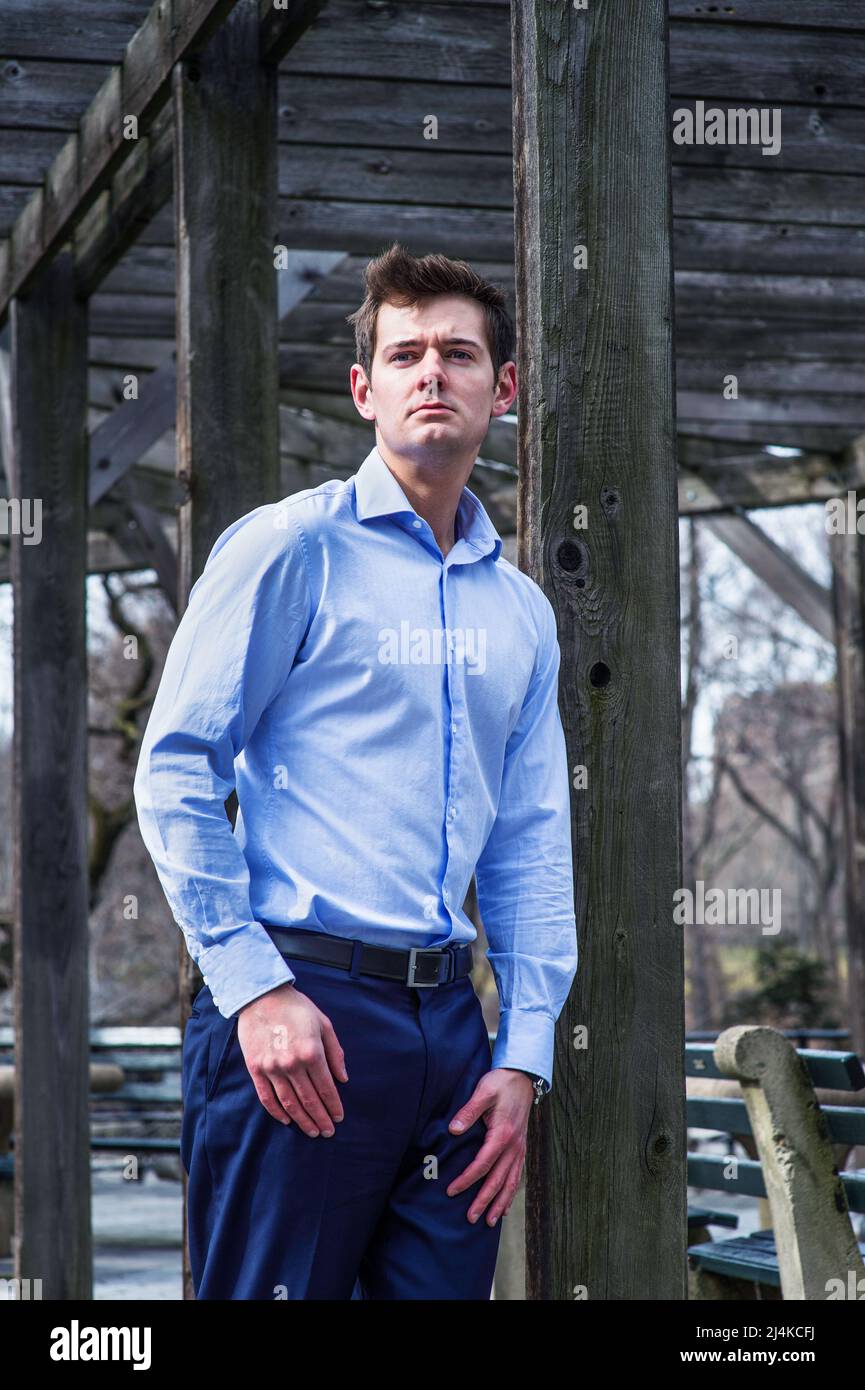 A young guy, standing by a wooden fame, is looking forward and deeply