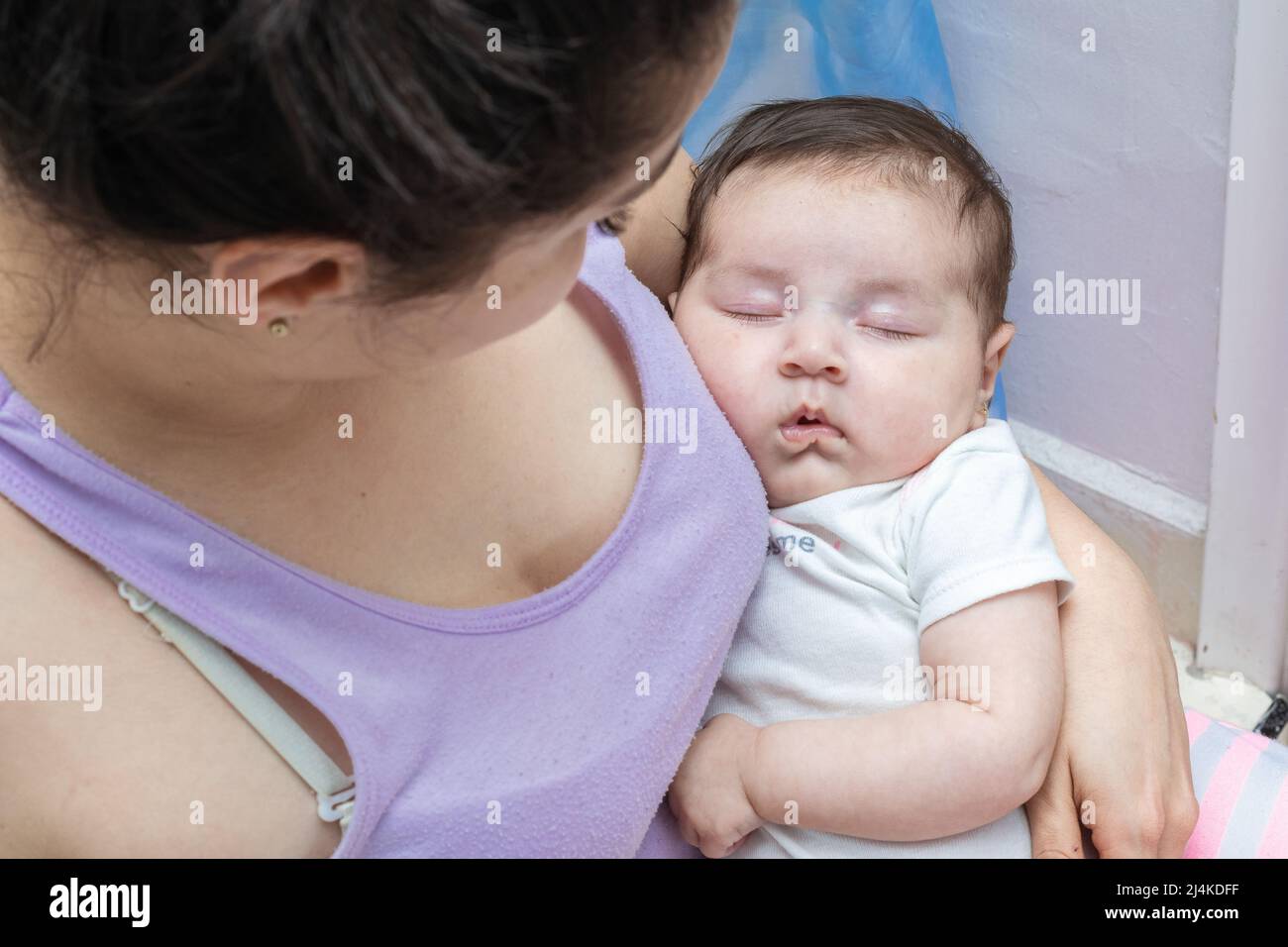 latin mother looking at her baby as she sleeps tenderly in her arms