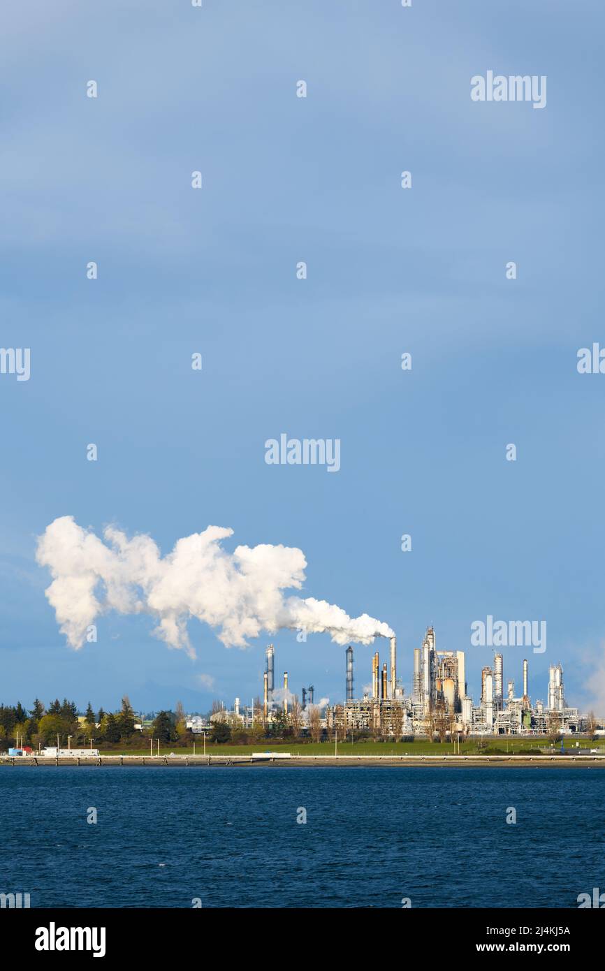 Steam from a industrial plant rising in to a blue cloudy sky.  The steam drifts above the complex Stock Photo