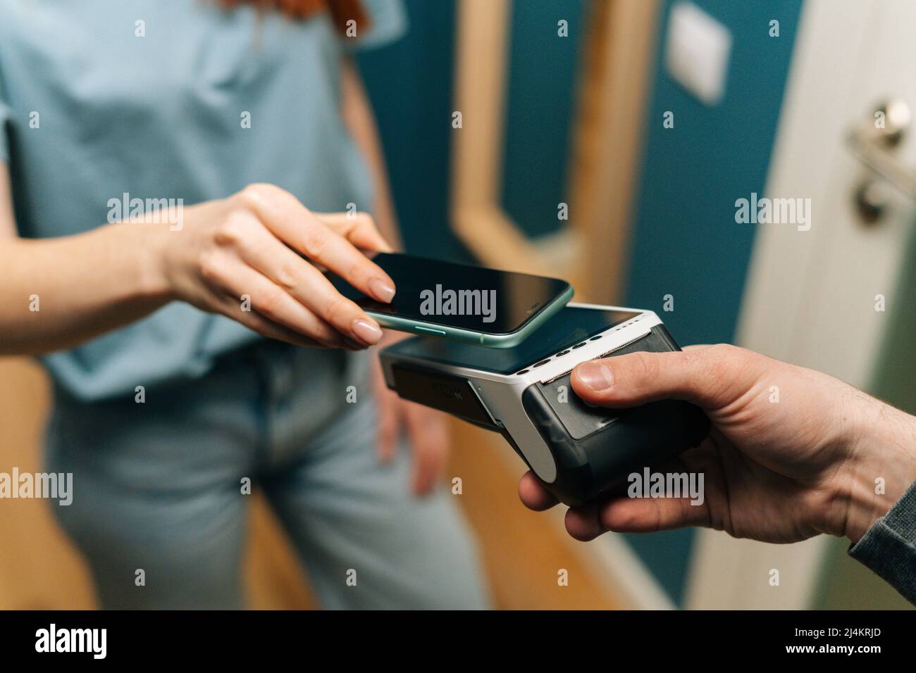 Close-up high-angle view of unrecognizable courier male giving POS wireless terminal to making contactless payment using mobile phone to young female Stock Photo