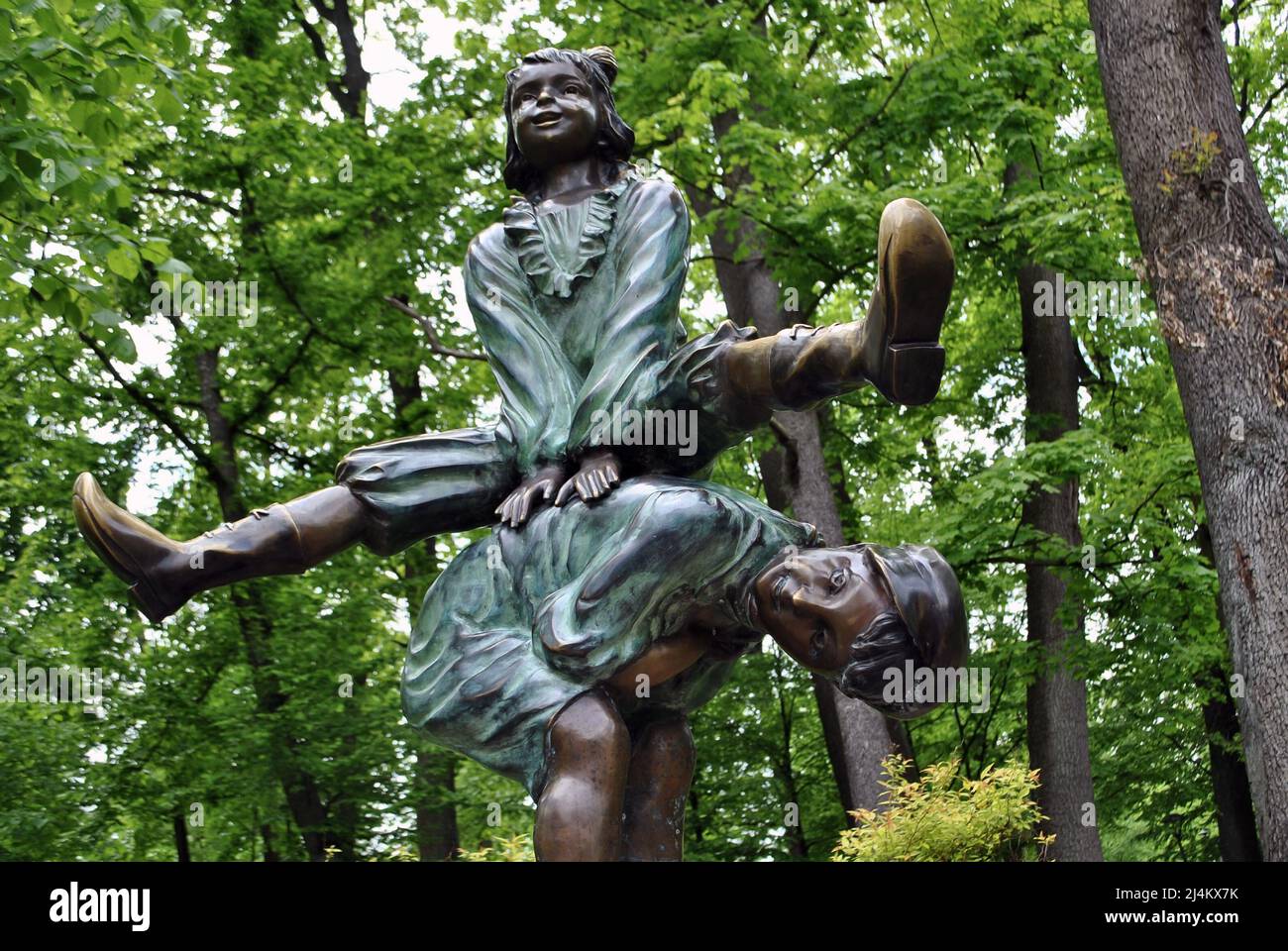 Bronze sculpture in the form of a playing girl jumping over a tilted boy against the background of trees in the park Stock Photo