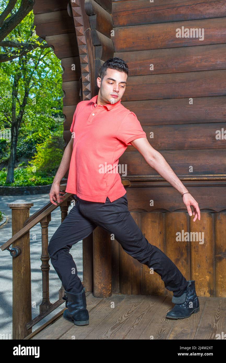 Dressing in a red Polo shirt, black pants and leather boots, stretching arms and turning over legs,  a young handsome guy is standing by an old fashio Stock Photo