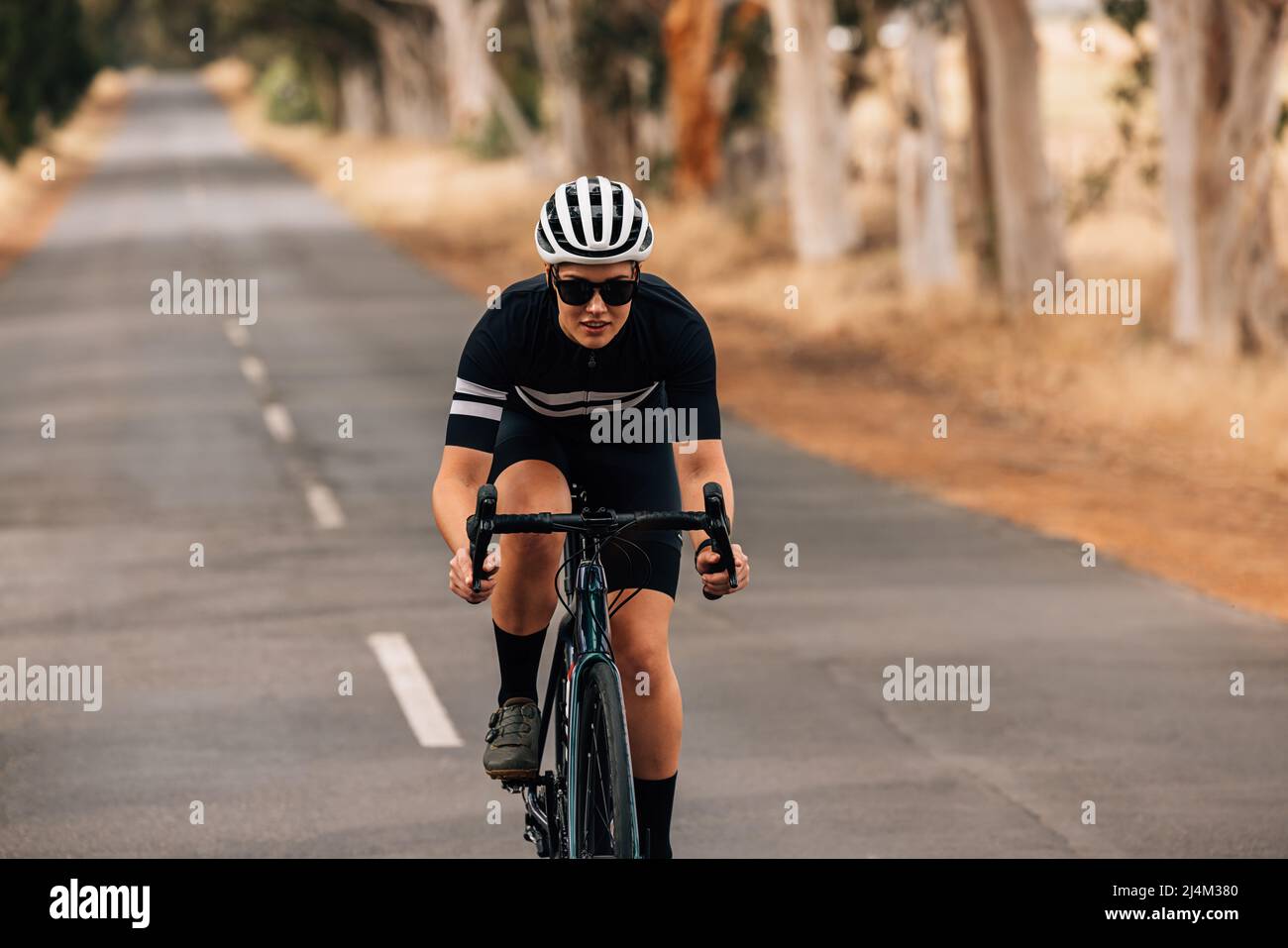 Pro bike female rider wearing helmet and sunglasses training outdoors on empty countryside road Stock Photo