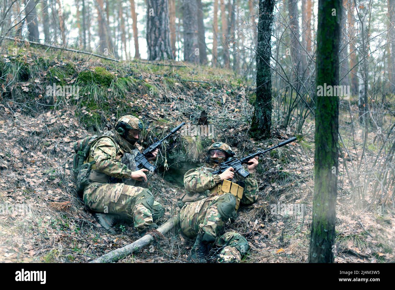 Two mercenaries in an ambush during a special operation in the forest. They hide from the enemy before attacking. Collage - one model in two poses. Stock Photo