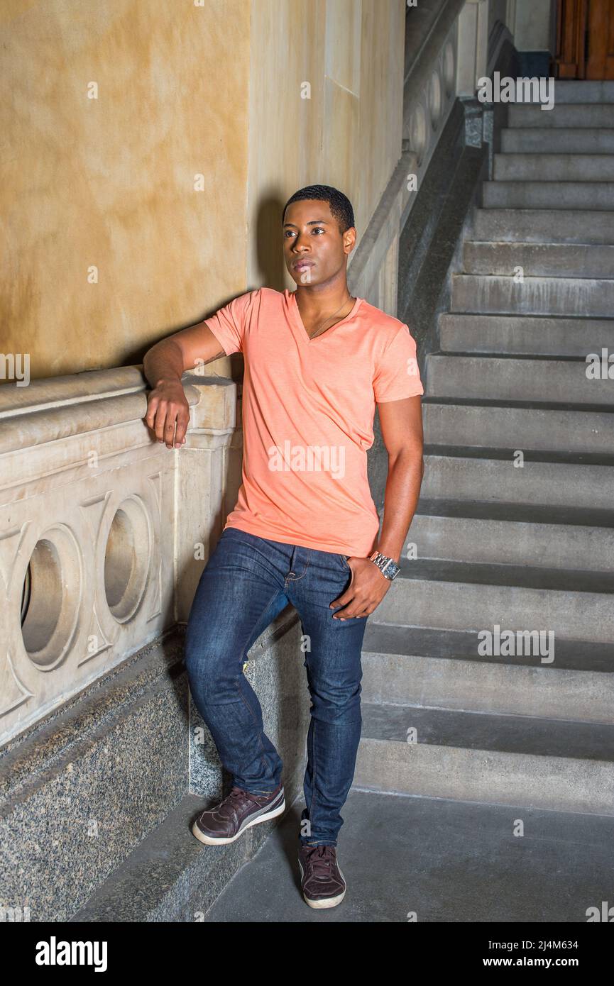 Dressing in a light orange short sleeve V neck shirt, jeans and leather  sneakers, a young handsome black student is standing downstairs by railing  in Stock Photo - Alamy