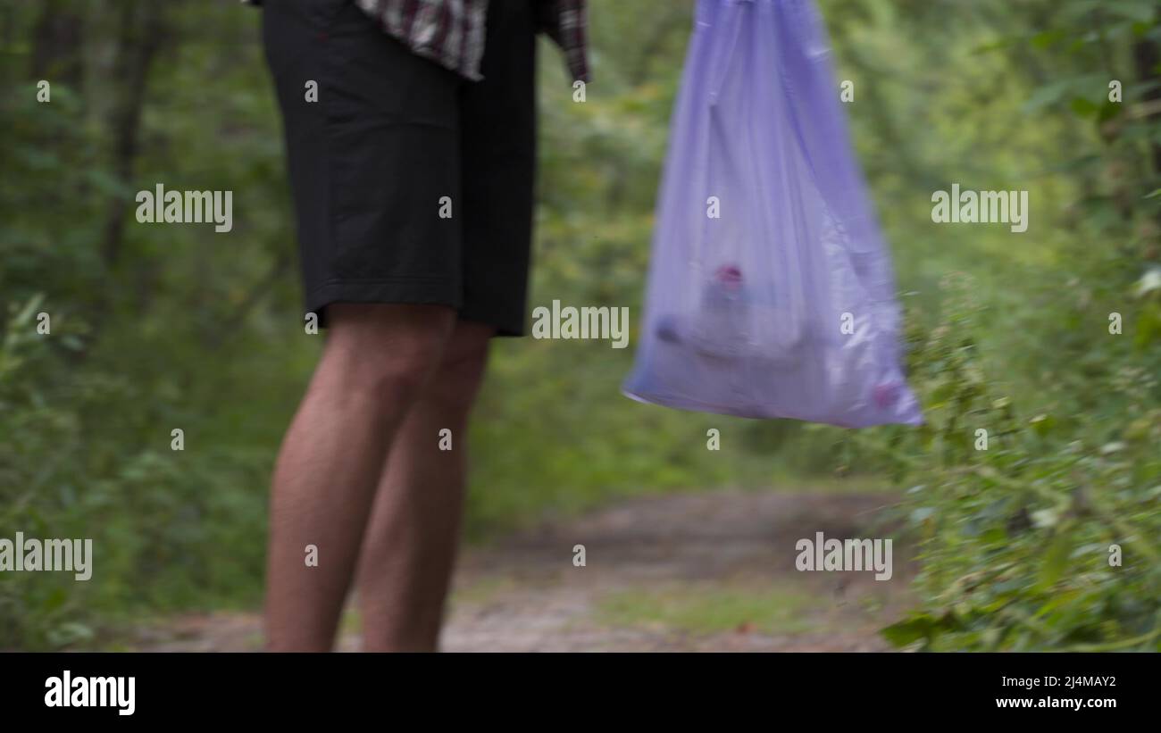 Young man throwing litter garbage from plastic bag on ground. Environmental pollution. Global warming. Male throwing out garbage in forest. Ecological Stock Photo