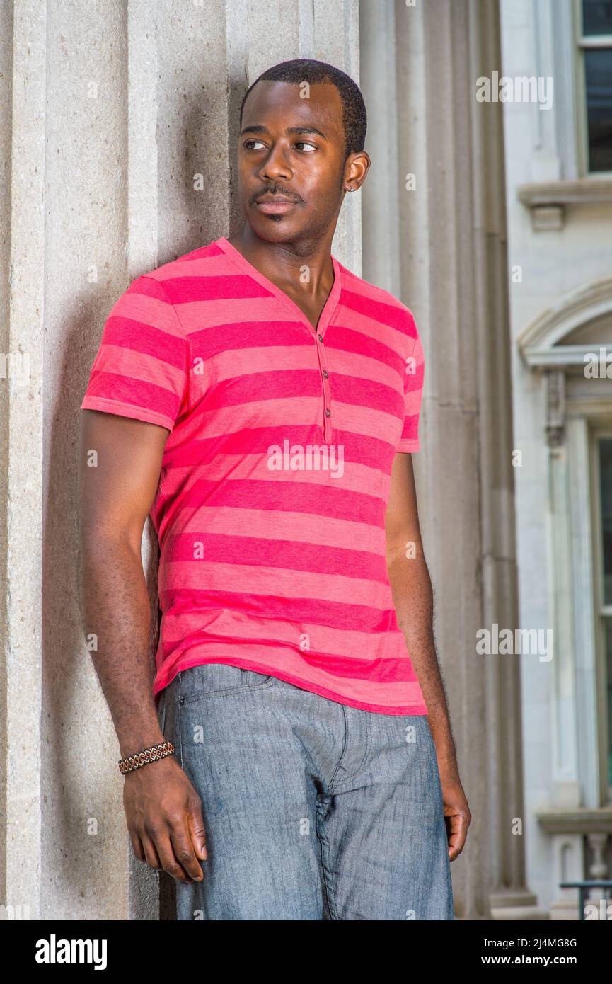 Dressing red, pink stripe Henley V Neck T shirt, gray pants, wearing a bracelet, a young black guy is standing by a pillar, confidently looking fo Stock Photo - Alamy