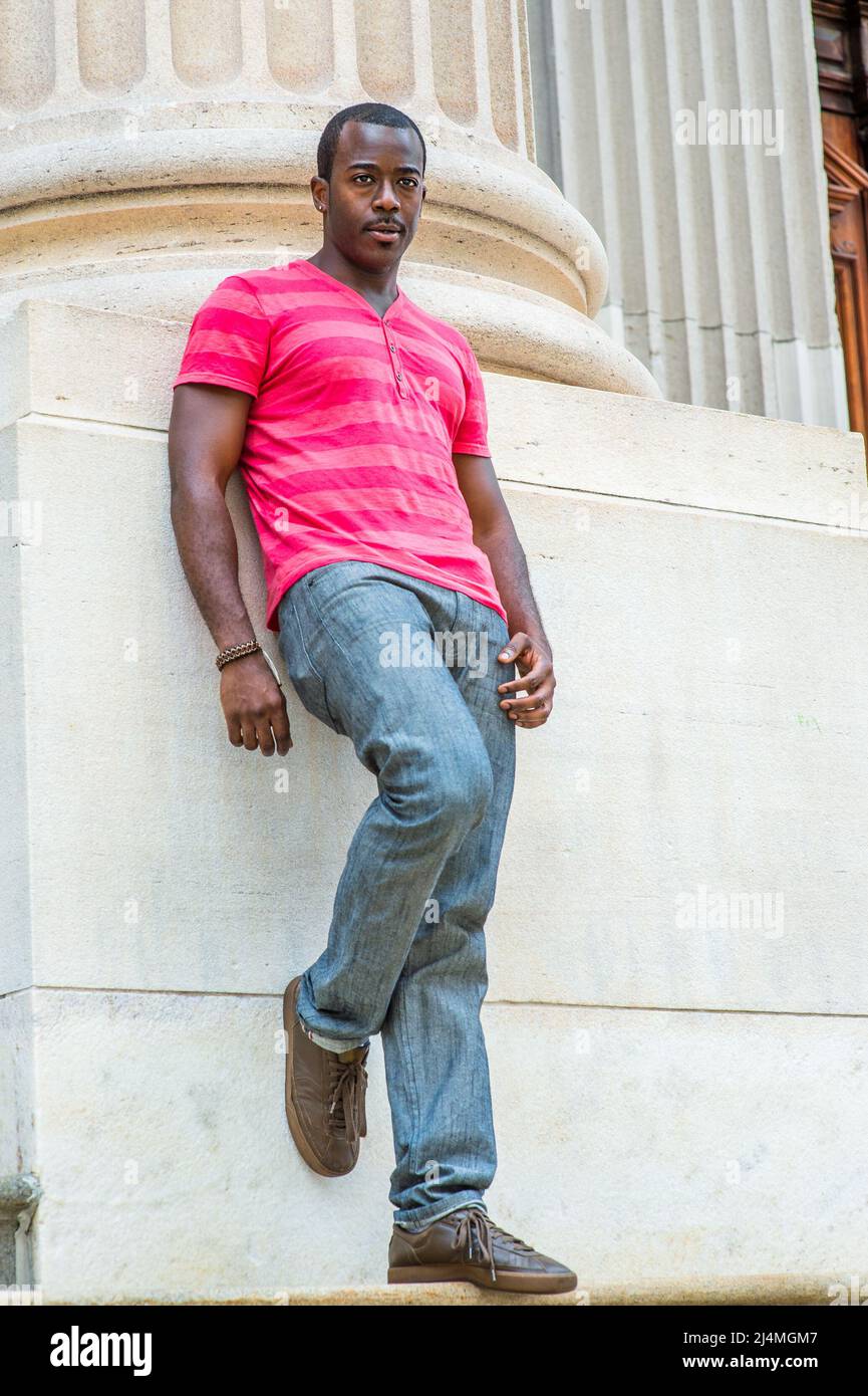 Wearing a pink stripe Henley V T shirt, gray pants, sneakers, bending over a leg, a young black guy is standing against the base of Stock Photo - Alamy