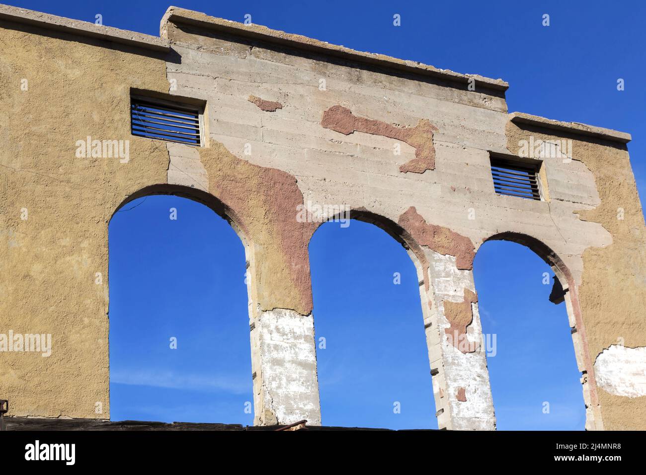 Old Grocery Store Ruin Exterior with Crumbling Facade Arch in Front of Art Studio against Blue Sky Background in Jerome Arizona City Main Street Stock Photo