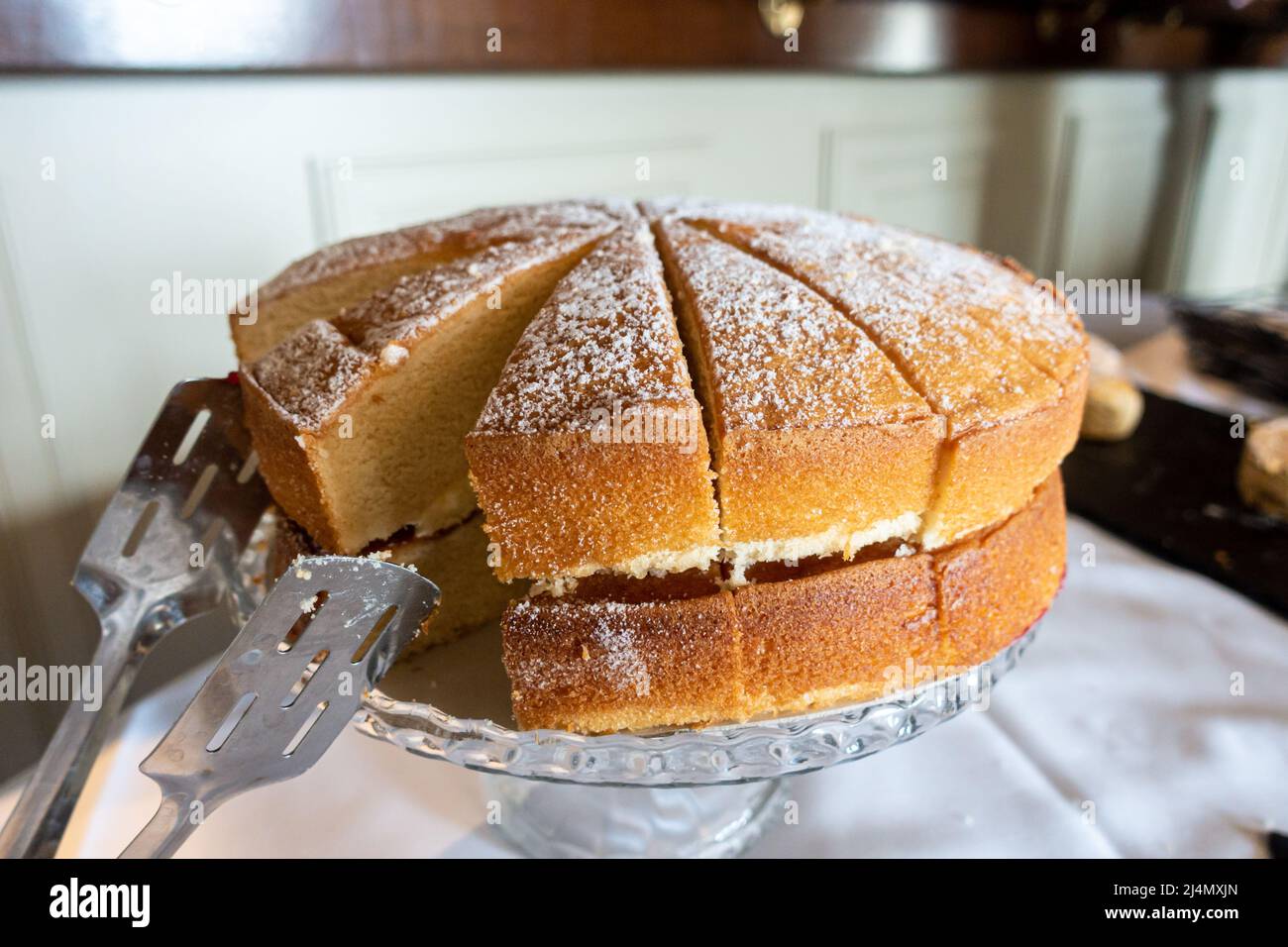 A Victoria sponge cake filled with butter icing and jam has been cut into slices ready for serving. Stock Photo