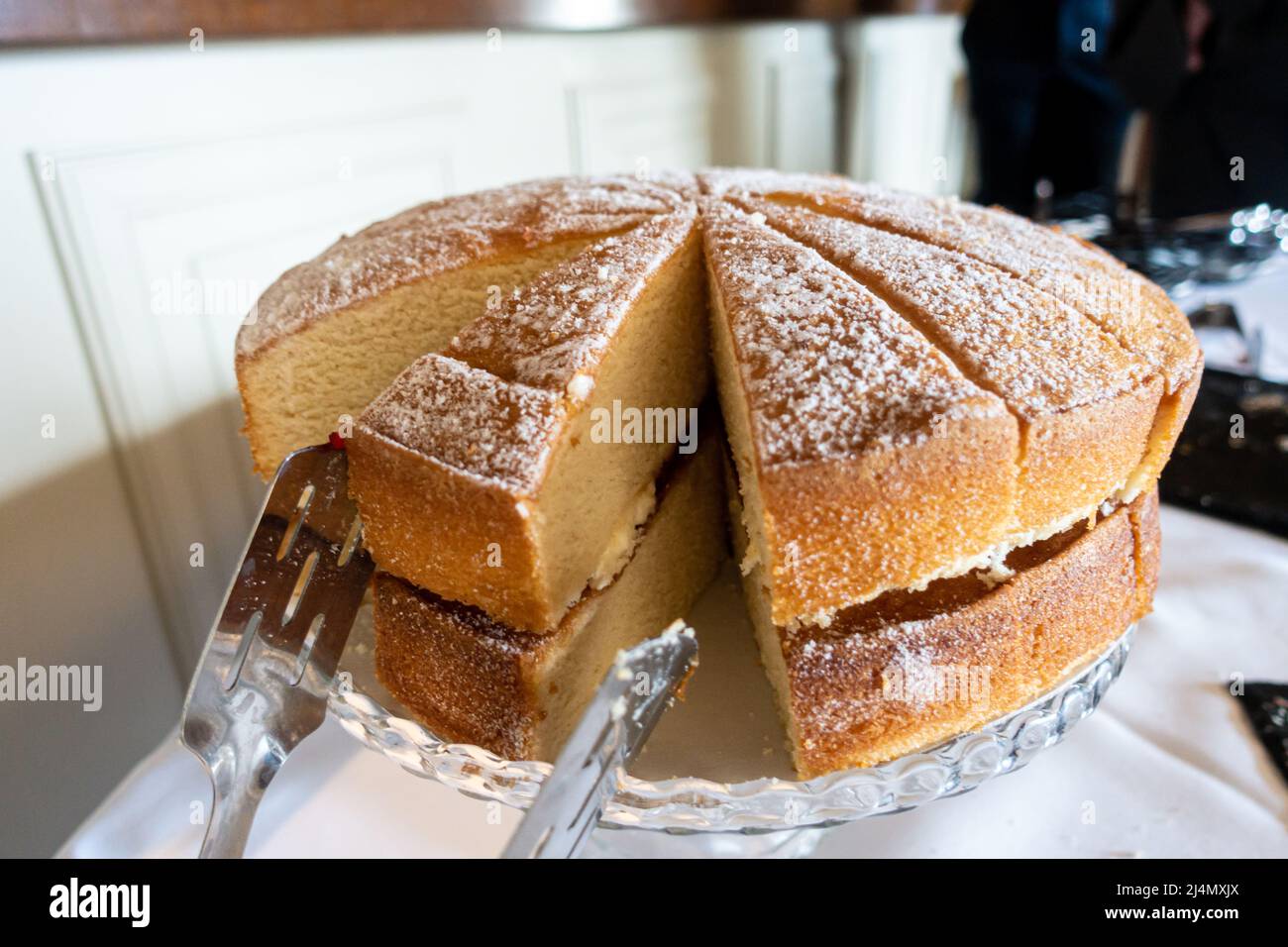 A Victoria sponge cake filled with butter icing and jam has been cut into slices ready for serving. Stock Photo