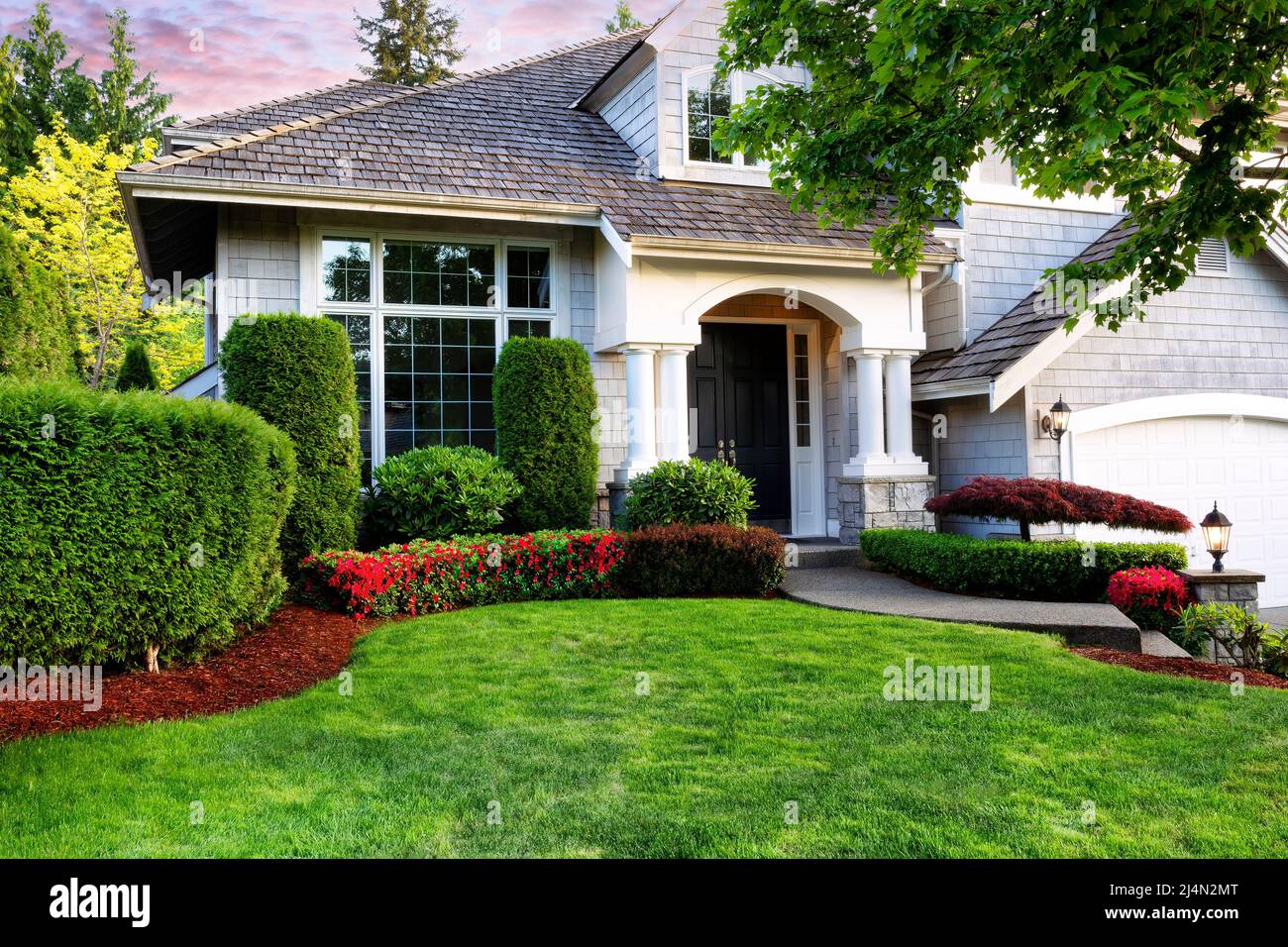 Beautiful home exterior in evening with manicured green lawn and blooming red flowers in bushes Stock Photo