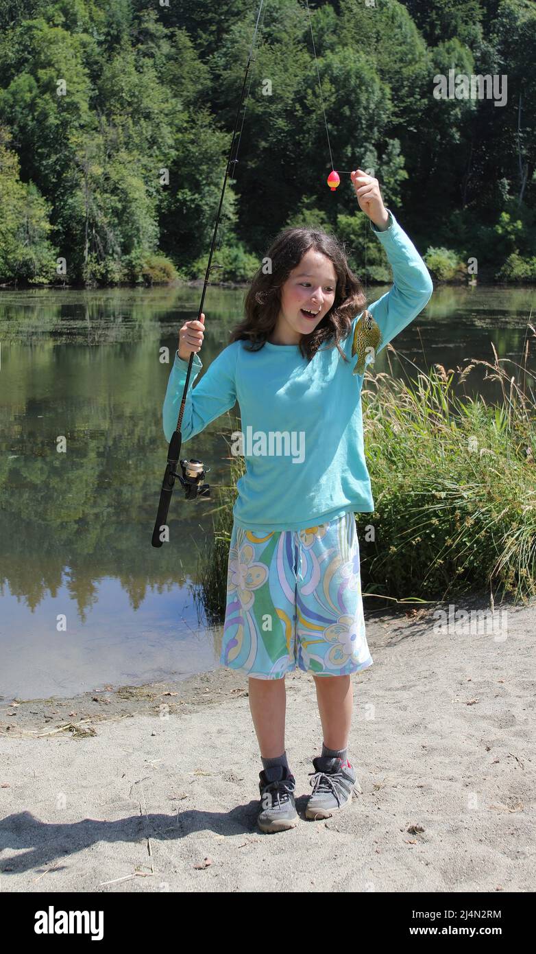 Young girl smiling at her first fish caught while fishing in a small pond from shore Stock Photo