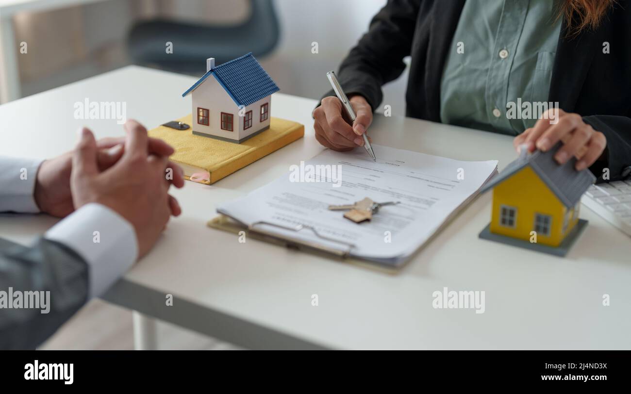 Real estate agent assisting client to sign contract at desk with house