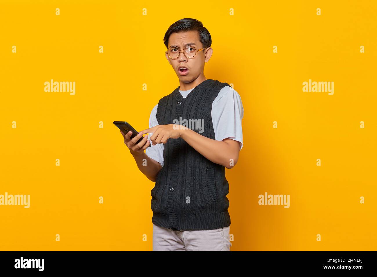 Surprised handsome young man using and texting smartphone on yellow background Stock Photo