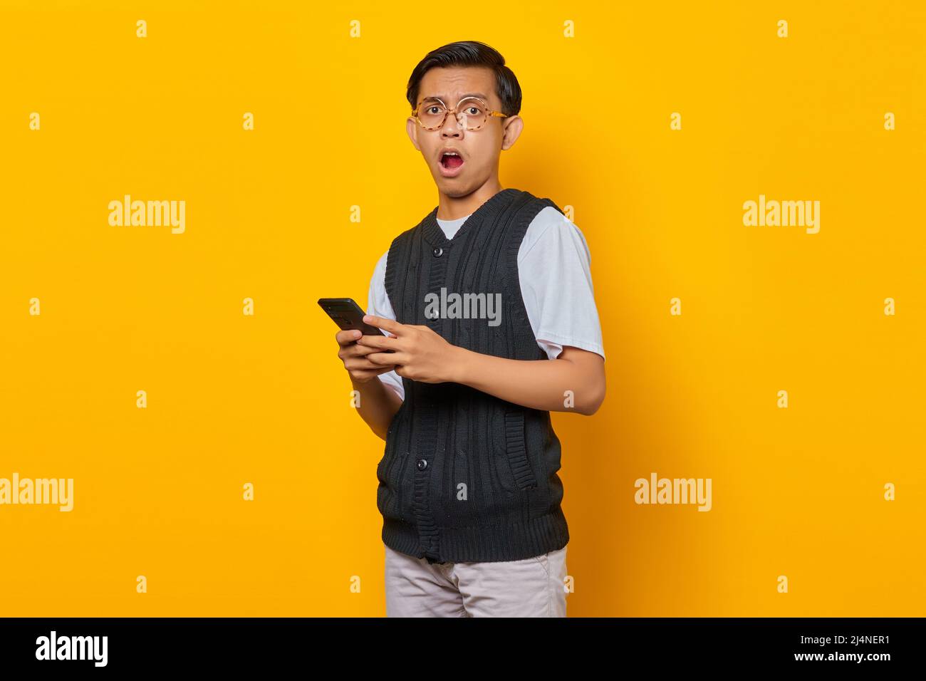 Portrait of a surprised handsome young man using smartphone on yellow background Stock Photo