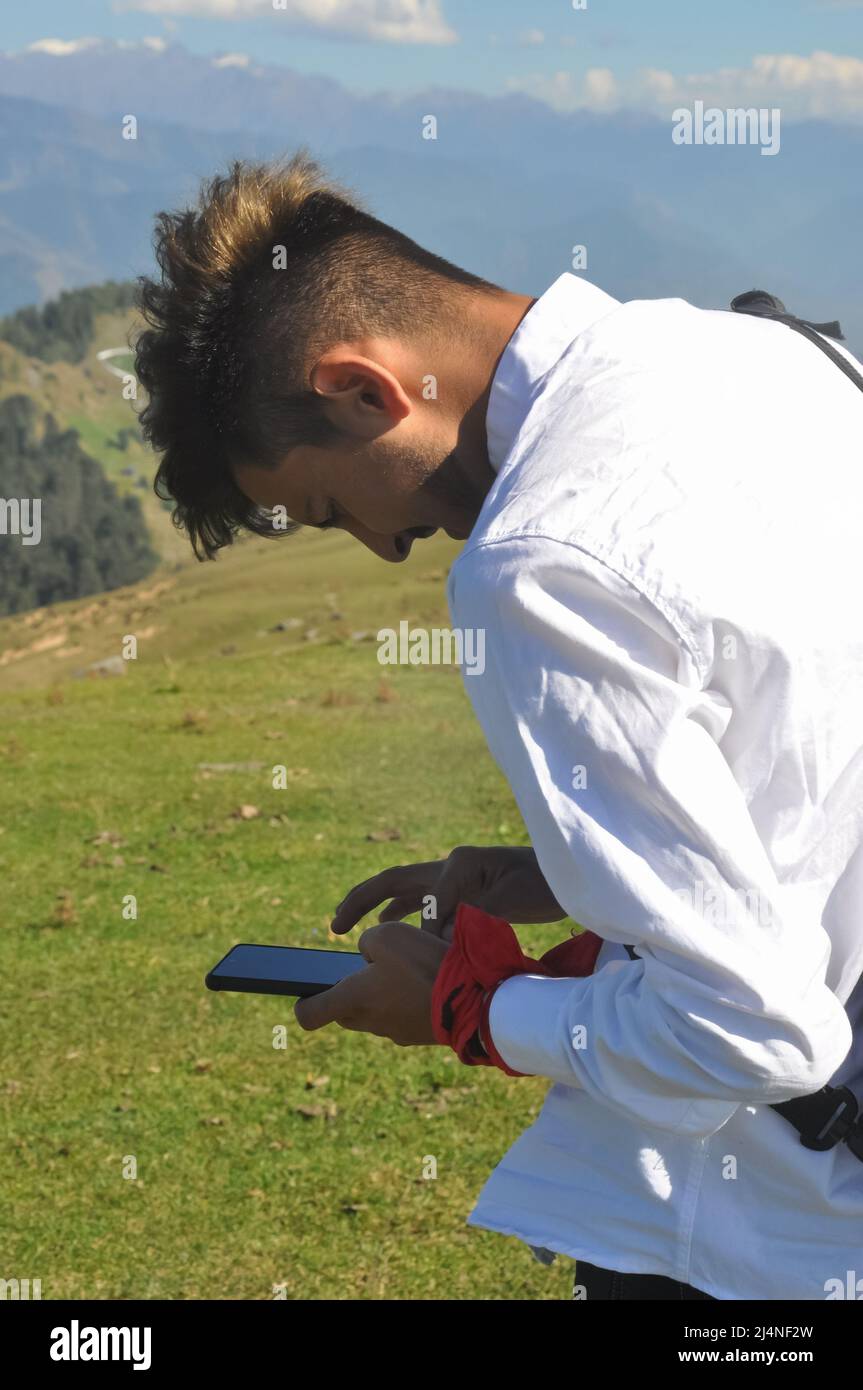 Side view of a young guy using his phone in the mountain Stock Photo