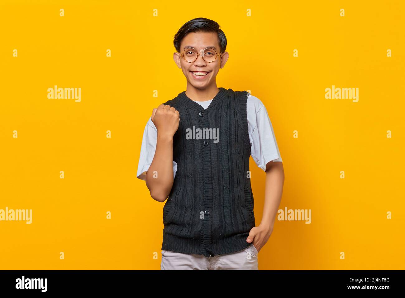 Portrait of excited young Asian man celebrating success with raised arms on yellow background Stock Photo