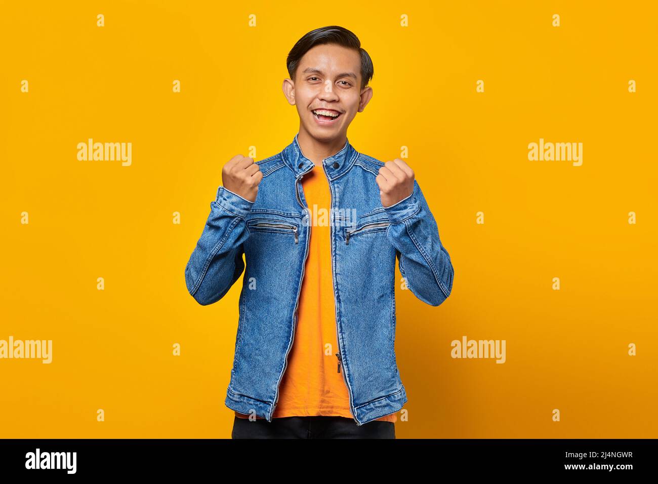 Portrait of excited young Asian man celebrating success with raised hands isolated on yellow background Stock Photo