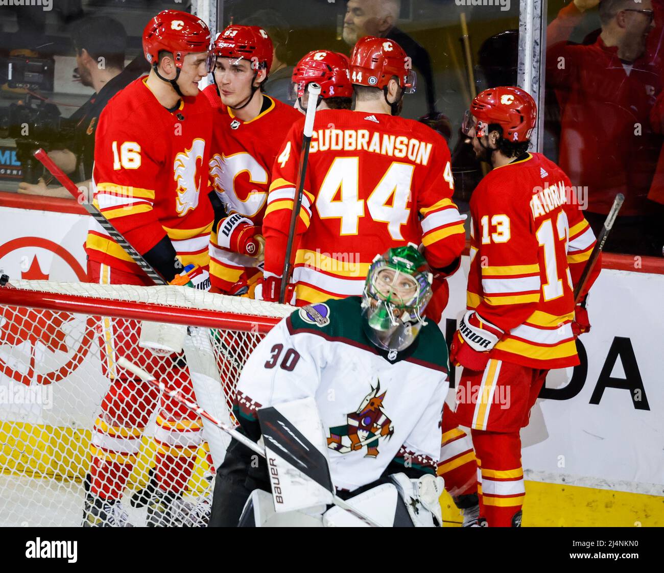 April 16, 2022, Calgary, AB, CANADA: Arizona Coyotes' Nathan Smith, left,  is checked by Calgary Flames' Rasmus Andersson, centre, as goalie Jacob  Markstrom blocks the net during third period NHL hockey action