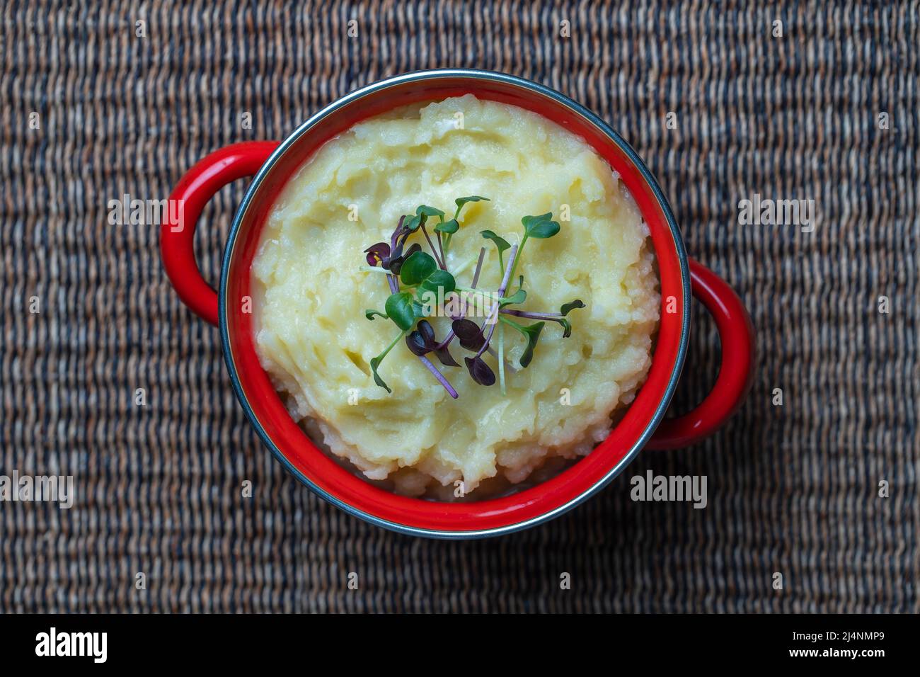 Mashed potatoes with radish microgreens in a red saucepan close up, top view Stock Photo