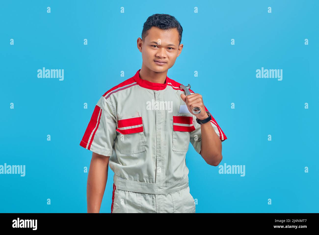 Image of smiling Asian handsome man wearing mechanical uniform holding wrench isolated on blue background Stock Photo