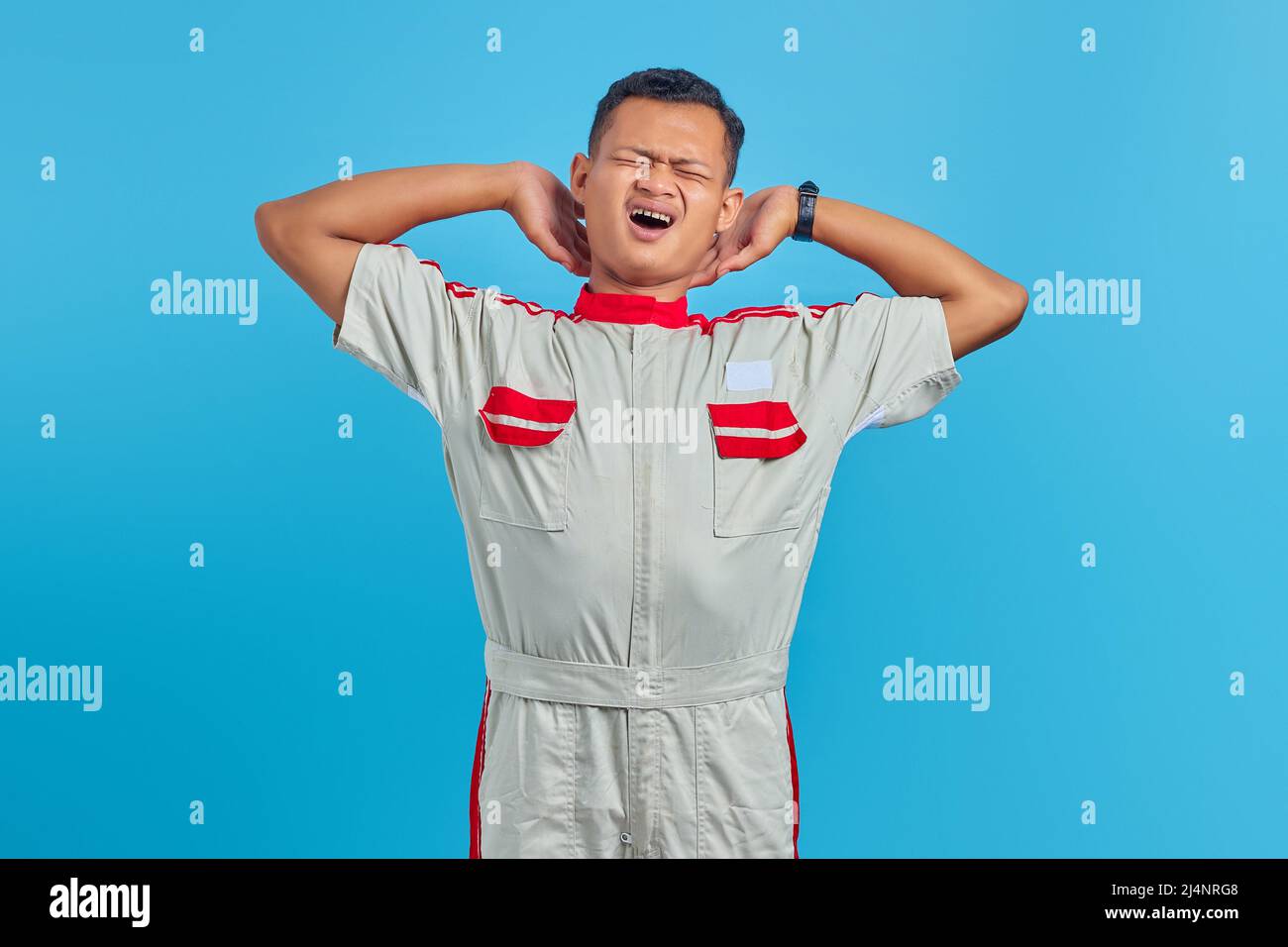 Portrait of young Asian mechanic feeling sleepy with mouth open over blue background Stock Photo