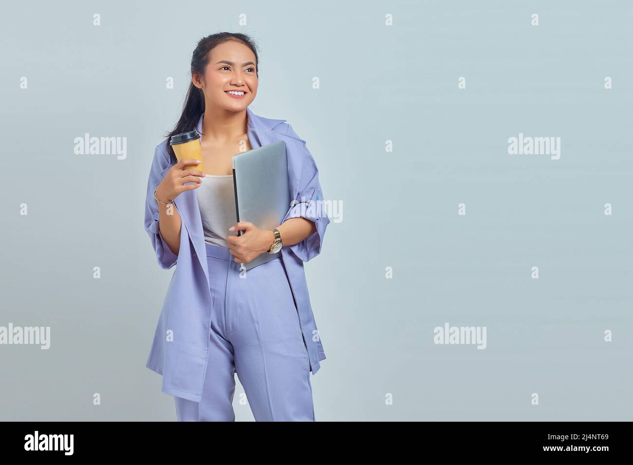 Portrait of cheerful young Asian woman holding laptop and coffee ...