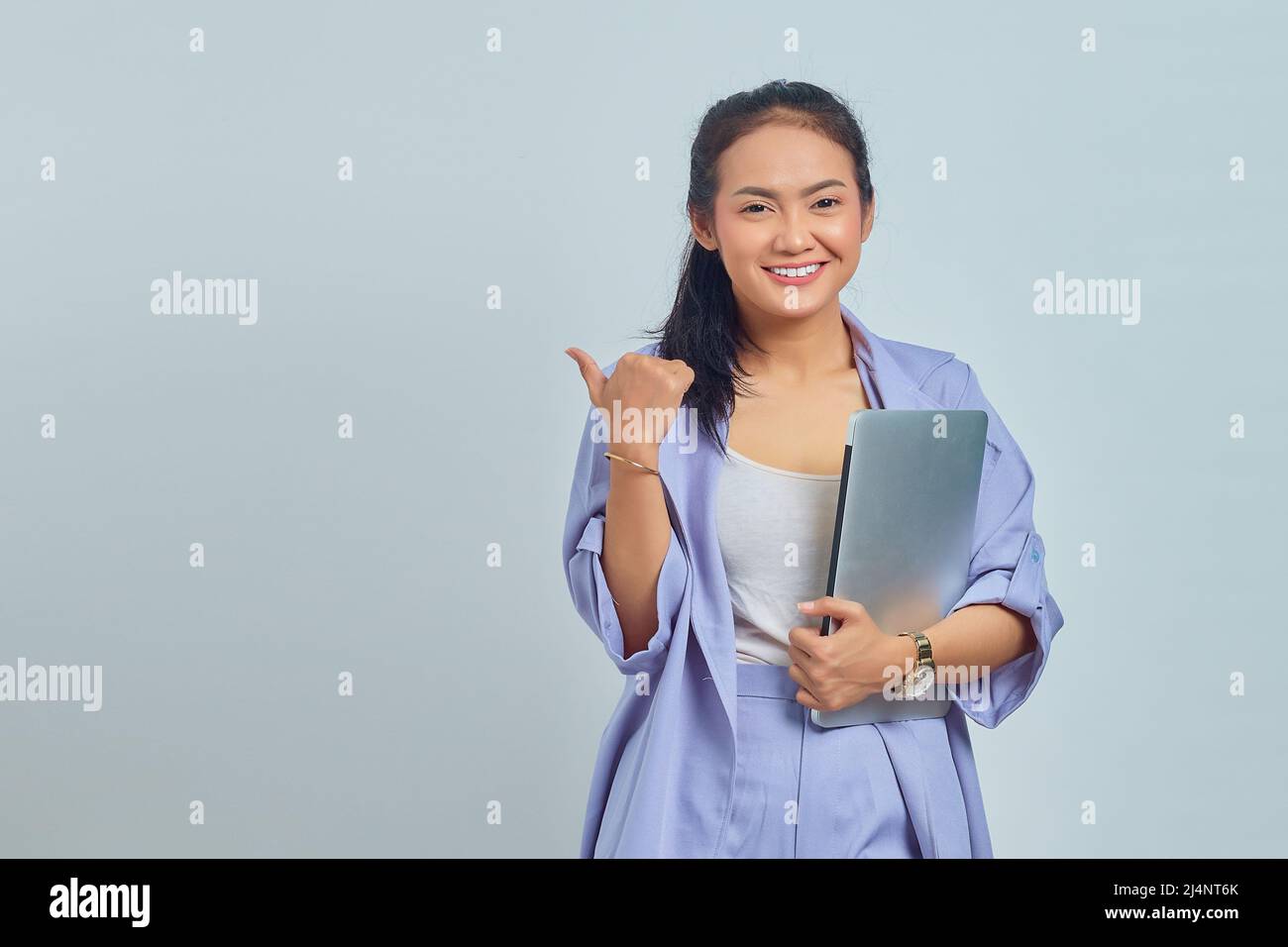 Portrait of smiling young asian woman holding a laptop and showing ...
