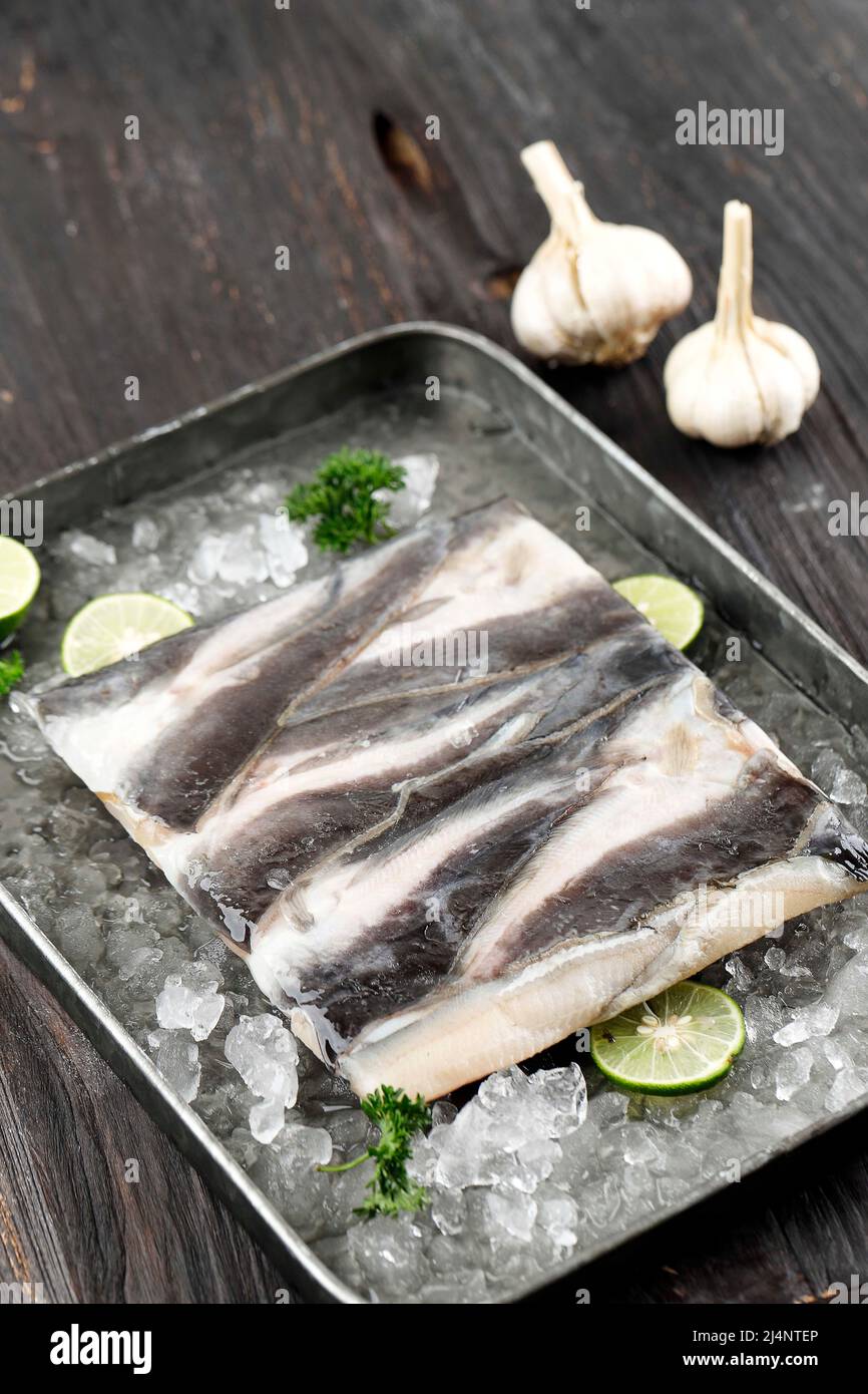 Frozen Catfish Fillet Lele Filet on Tray with Sliced Lime and Crushed Ice, Soft Focus on Wooden Table Stock Photo