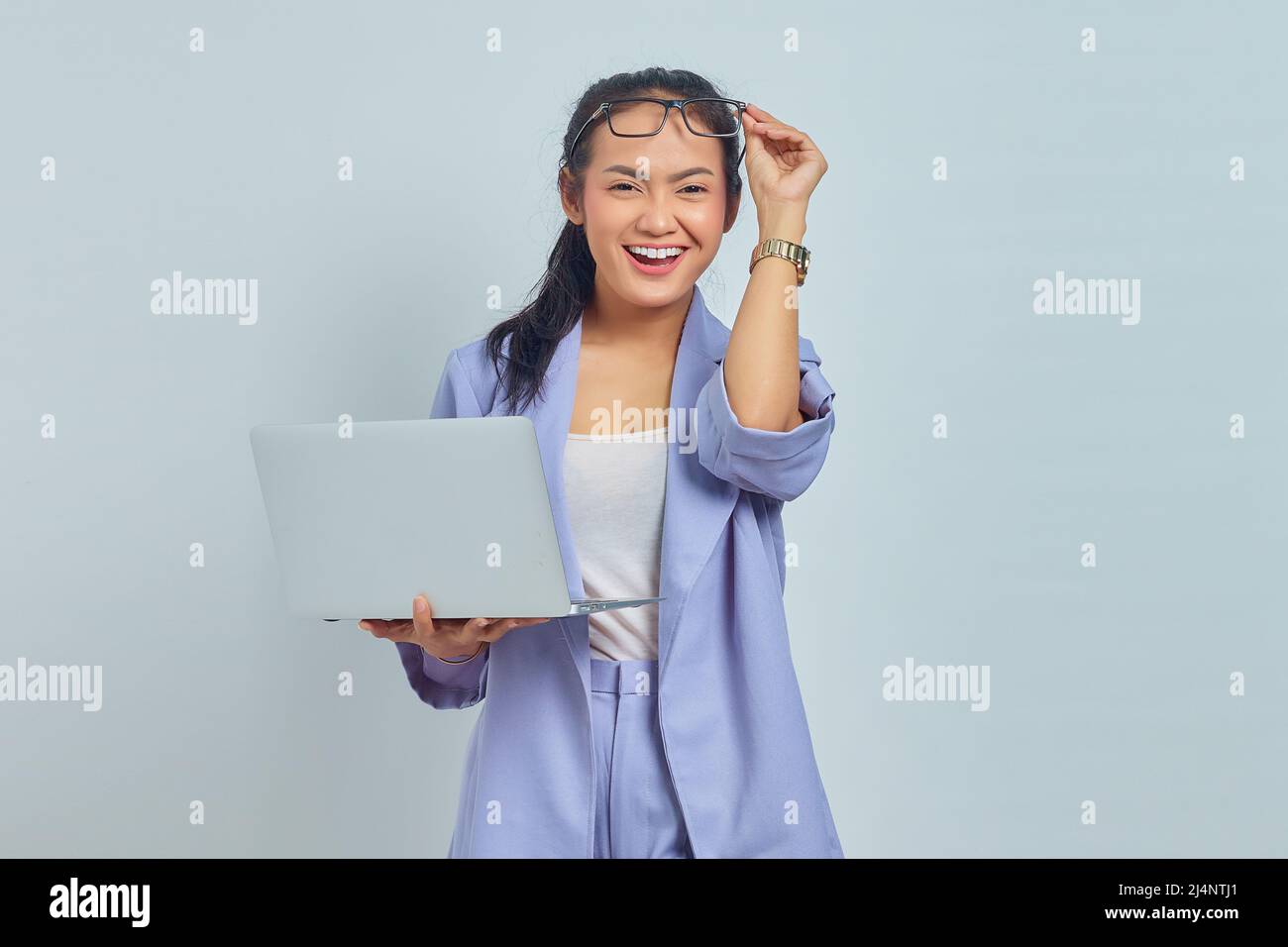 Portrait of cheerful young Asian woman holding laptop and taking off ...