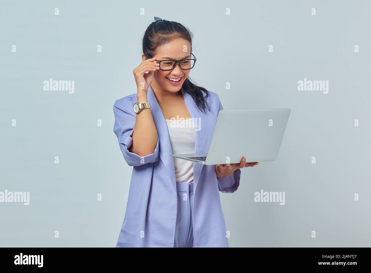 Portrait of cheerful young Asian woman holding laptop and taking off ...