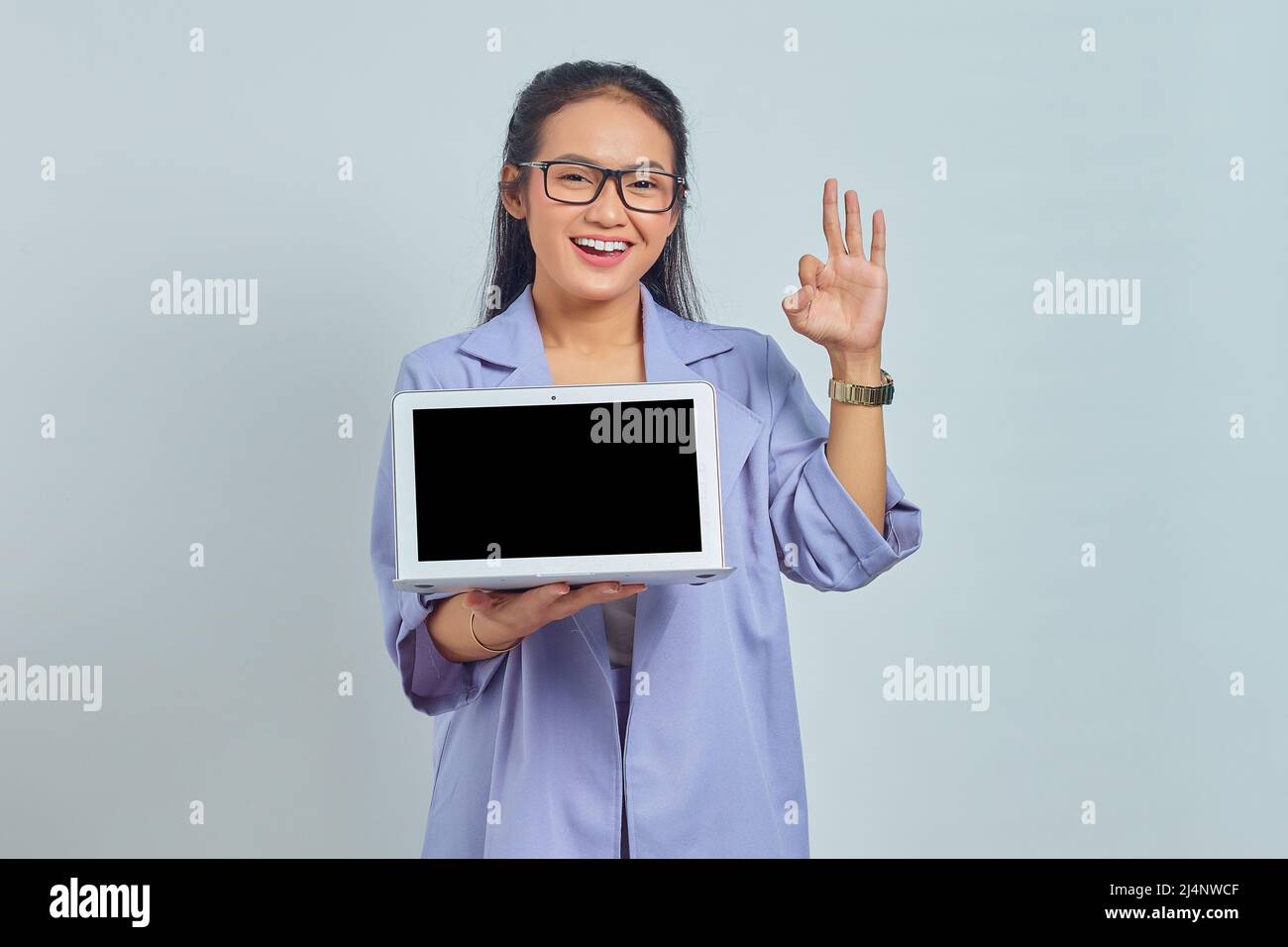 Portrait of cheerful young Asian woman showing blank laptop screen and ...