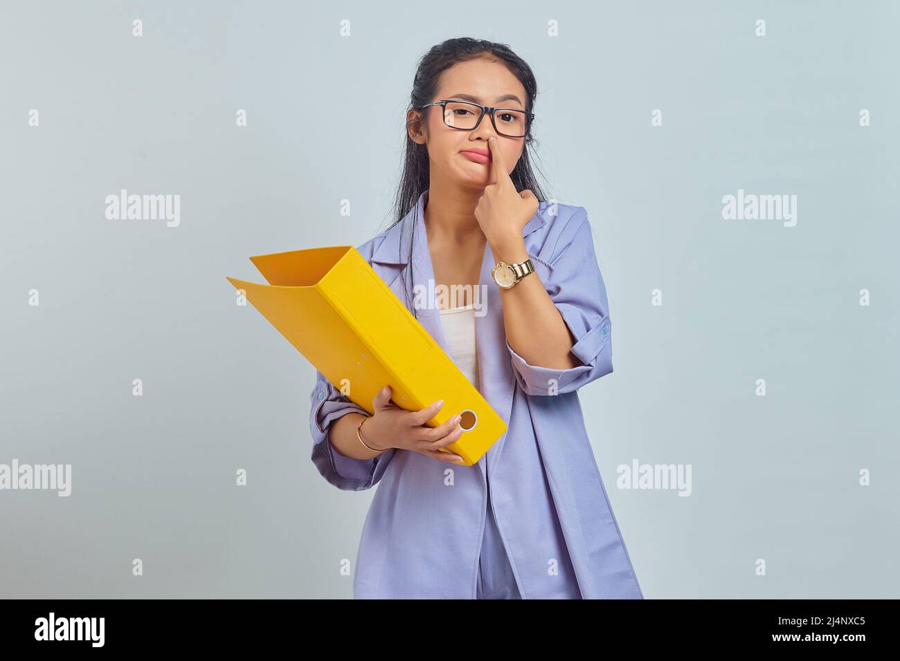 Portrait of funny young Asian woman thinking about something while carrying yellow folder and  picking her nose isolated on yellow background Stock Photo
