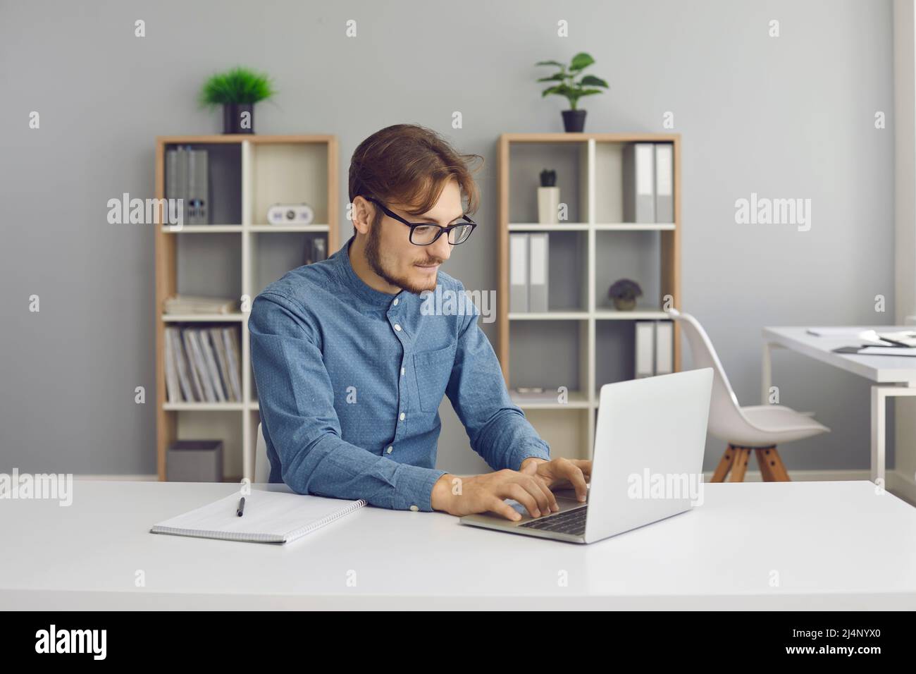 Happy student or office worker sitting at desk and working on his laptop computer Stock Photo