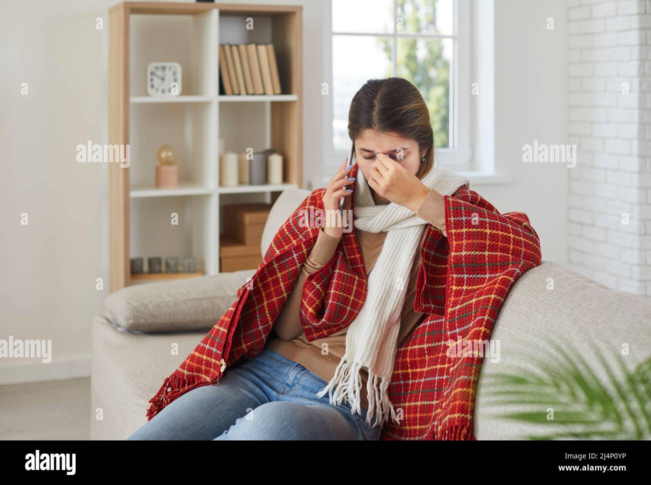 Woman who has caught cold or flu sitting on couch at home and talking to doctor on phone Stock Photo