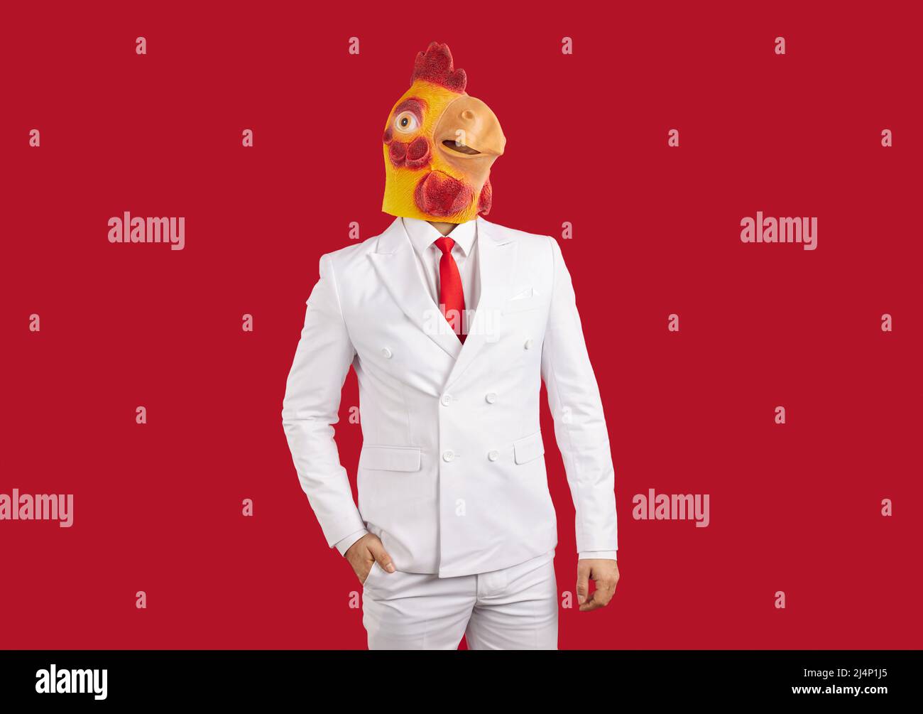 Portrait of man in white suit and funny chicken mask standing against red background Stock Photo