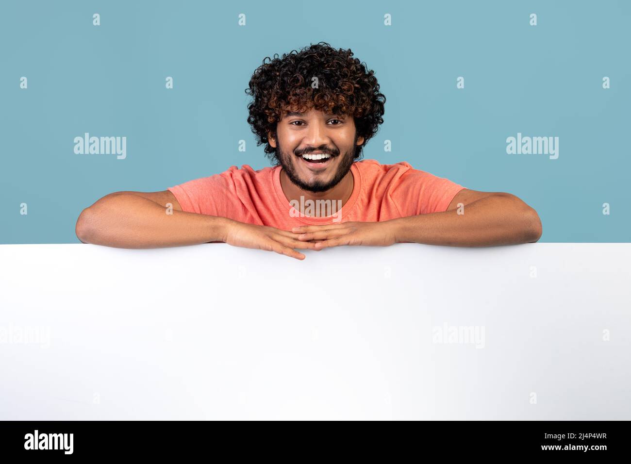 Relaxed bearded indian guy leaning on empty board for advertisement Stock Photo