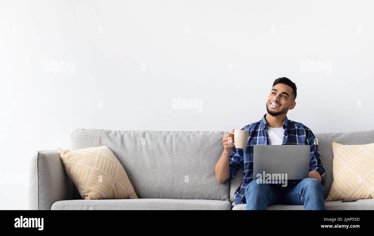 Man using pc sitting on the couch, drinking coffee Stock Photo