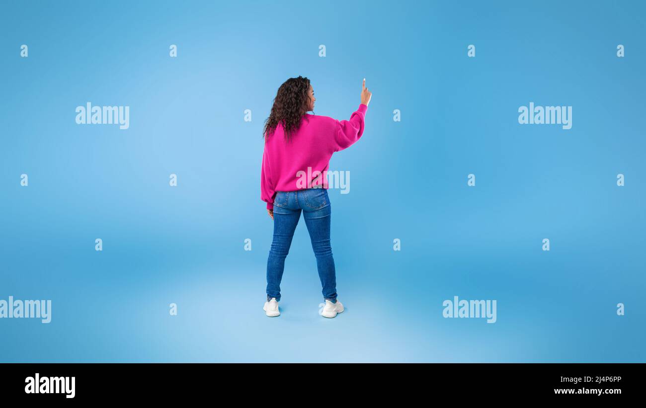 Back view of millennial African American lady touching imaginary screen, pressing button, using virtual interface Stock Photo