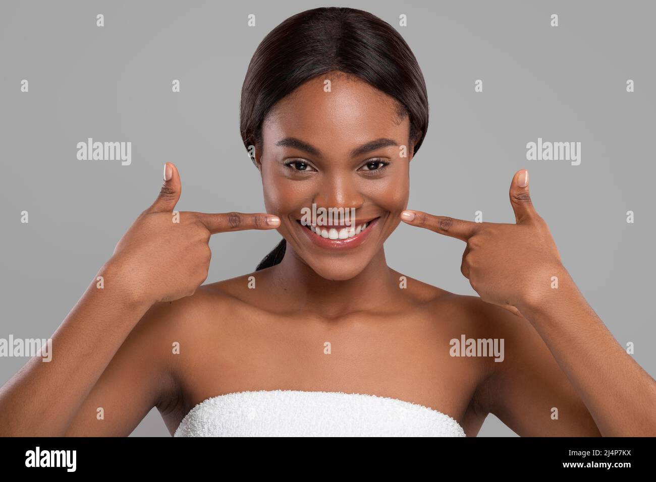 Cheerful pretty black woman wrapped in towel pointing fingers at perfect snow white smile Stock Photo