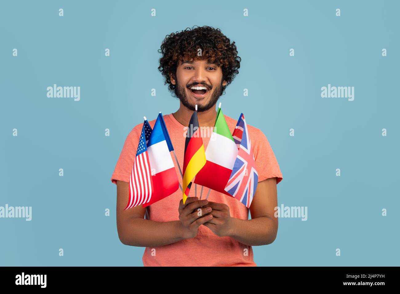 Happy hindu guy holding diverse flags, blue studio background Stock Photo